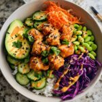 A vibrant bowl of Bang Bang Salmon Bites Bowls featuring crispy salmon bites, rice, avocado, cucumber, edamame, shredded carrots, and red cabbage.