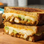 A close-up of a stacked CHICKEN AVOCADO MELT SANDWICH with melted cheese and avocado slices.