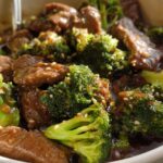 Close-up shot of tender beef and vibrant broccoli florets coated in a savory sauce, sprinkled with sesame seeds. Chinese Beef and Broccoli.