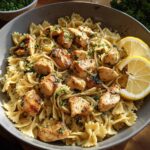A bowl of Cowboy Butter Lemon Bowtie Chicken Pasta with broccoli, garnished with lemon slices and parsley.