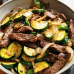 A close-up of a Cozy Grilled Steak Bowl with tender steak slices, sautéed zucchini rounds, and onions.