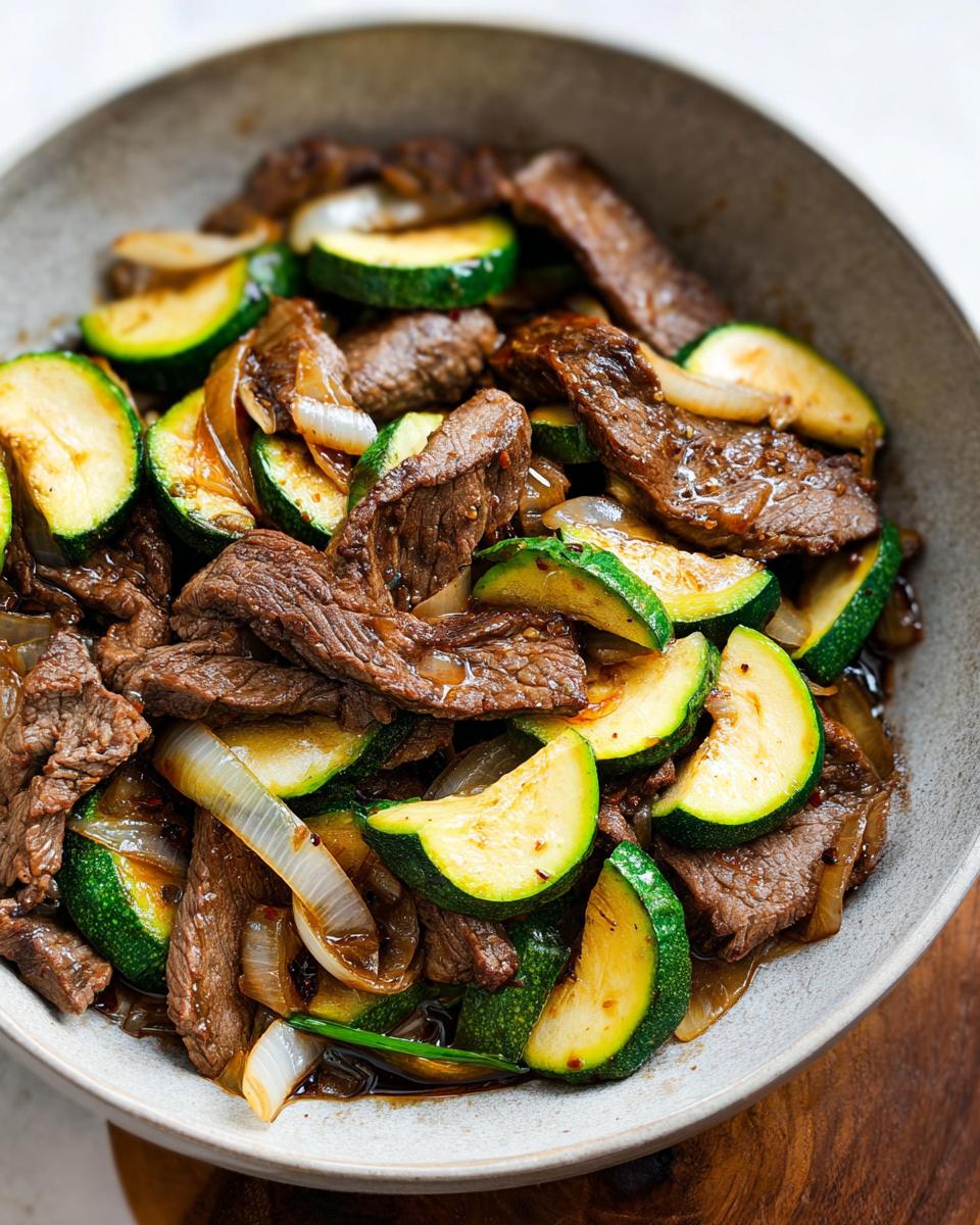 A close-up of a Cozy Grilled Steak Bowl with tender steak slices, zucchini rounds, and onions in a savory sauce.