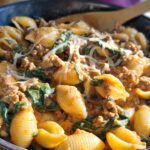 A close-up of creamy high protein beef pasta with shell pasta, spinach, and melted cheese.