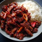A close-up of a bowl of Crispy Chilli Beef Rice, featuring glossy, spicy beef strips next to fluffy white rice.
