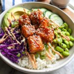 A delicious Crispy Salmon and Rice Bowl with avocado, edamame, cucumber, and red cabbage.