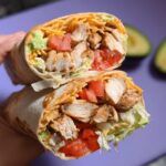 A halved Easy Chipotle Ranch Grilled Chicken Burrito filled with grilled chicken, lettuce, tomato, cheese, and avocado.