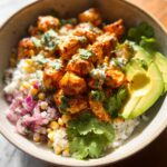 A close-up of an Easy Street Corn Chicken Bowl featuring seasoned chicken, rice, corn, red onion, avocado slices, and cilantro.