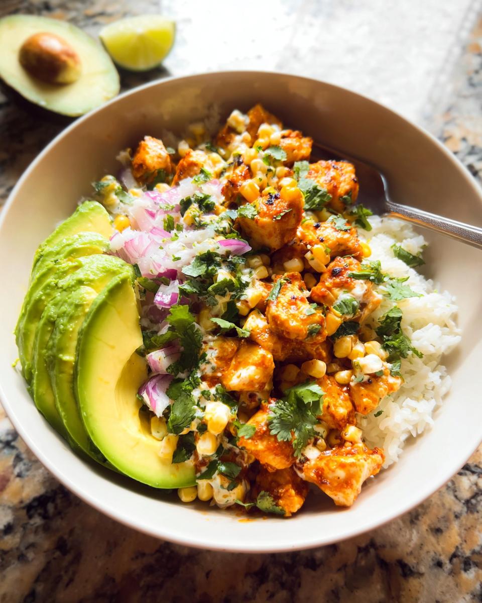 A close-up of an Easy Street Corn Chicken Bowl featuring seasoned chicken, corn, rice, avocado slices, and red onion.