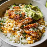 A close-up of an Easy Street Corn Chicken Bowl featuring sliced grilled chicken, corn, rice, crumbled cheese, and avocado.
