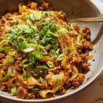 A close-up of a hearty bowl of Egg Roll in a Bowl, featuring ground meat, cabbage, and noodles, garnished with green onions and sesame seeds.