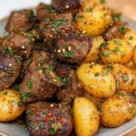 Close-up of delicious garlic steak bites and roasted potatoes, seasoned with herbs and chili flakes.