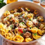 A close-up of a large bowl filled with Garlic Steak Tortellini, garnished with Parmesan cheese and parsley.