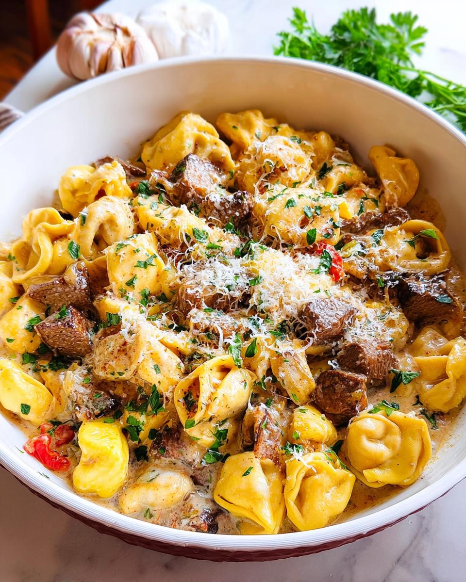 A close-up of Garlic Steak Tortellini in a creamy sauce, topped with grated Parmesan cheese and fresh parsley.