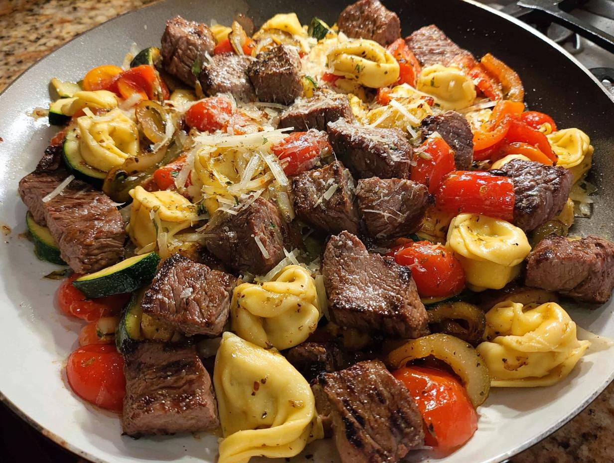 A close-up of a skillet filled with Garlic Steak Tortellini, featuring tender steak bites, cheese tortellini, zucchini, and cherry tomatoes.