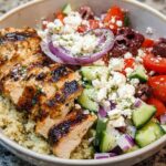 A close-up of Greek Chicken Bowls featuring grilled chicken, quinoa, cucumber, tomatoes, red onion, olives, and feta cheese.