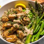 A healthy lemon garlic chicken meal prep bowl with quinoa, asparagus, peas, and a creamy sauce.