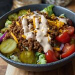 A delicious High-Protein Cheeseburger Bowl filled with seasoned ground beef, shredded cheese, lettuce, tomatoes, pickles, and a creamy sauce.