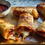 Golden brown HIGH PROTEIN Pepperoni Pizza Rolls with gooey melted cheese spilling out, served with a side of marinara sauce.