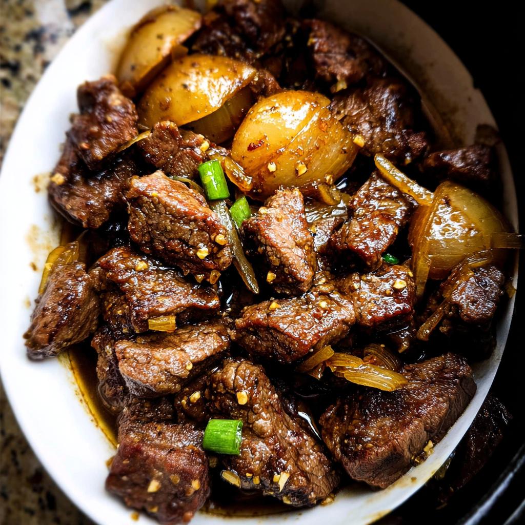 Close-up of tender High Protein Slow Cooker Garlic Butter Beef Bites with onions and green onions.