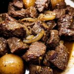 Close-up of tender High Protein Slow Cooker Garlic Butter Beef Bites with onions and potatoes in a savory sauce.