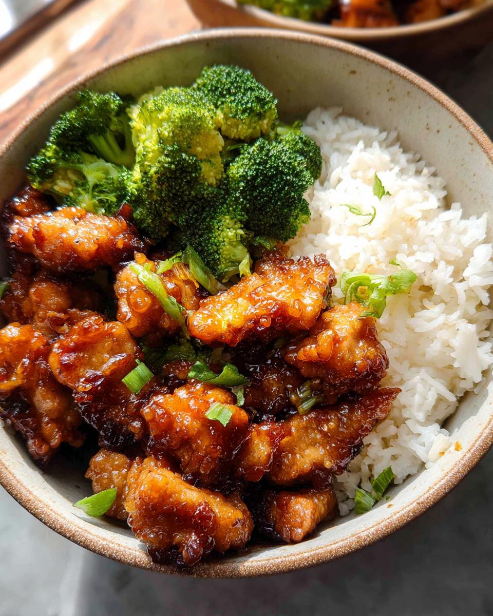 A close-up of a Honey Garlic Pork Rice Bowl featuring glazed pork, white rice, and steamed broccoli florets.