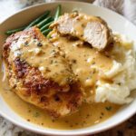 A plate of Irresistible Garlic Herb Chicken served with creamy mashed potatoes and green beans, drizzled with sauce.