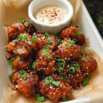 A close-up of Irresistible Sticky Honey Garlic Cauliflower bites, glazed and sprinkled with sesame seeds and green onions.