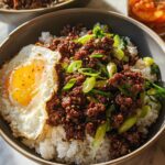 A close-up of a Korean Ground Beef Bowl served over white rice, topped with a fried egg and green onions.