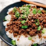 A close-up of a Korean Ground Beef Bowl, featuring seasoned ground beef over white rice, topped with sesame seeds and chopped green onions.