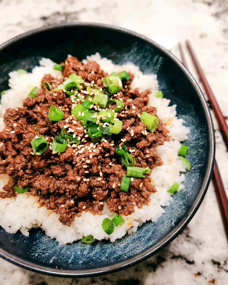 A close-up of a Korean Ground Beef Bowl, featuring seasoned ground beef over white rice, garnished with green onions and sesame seeds.