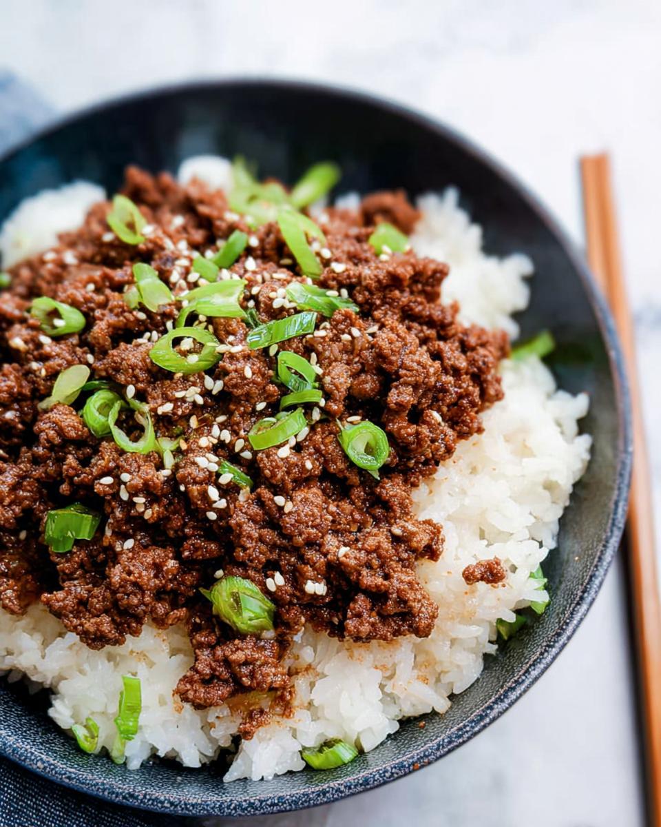 A close-up of a Korean Ground Beef Bowl, featuring seasoned ground beef over white rice, garnished with sesame seeds and chopped green onions.
