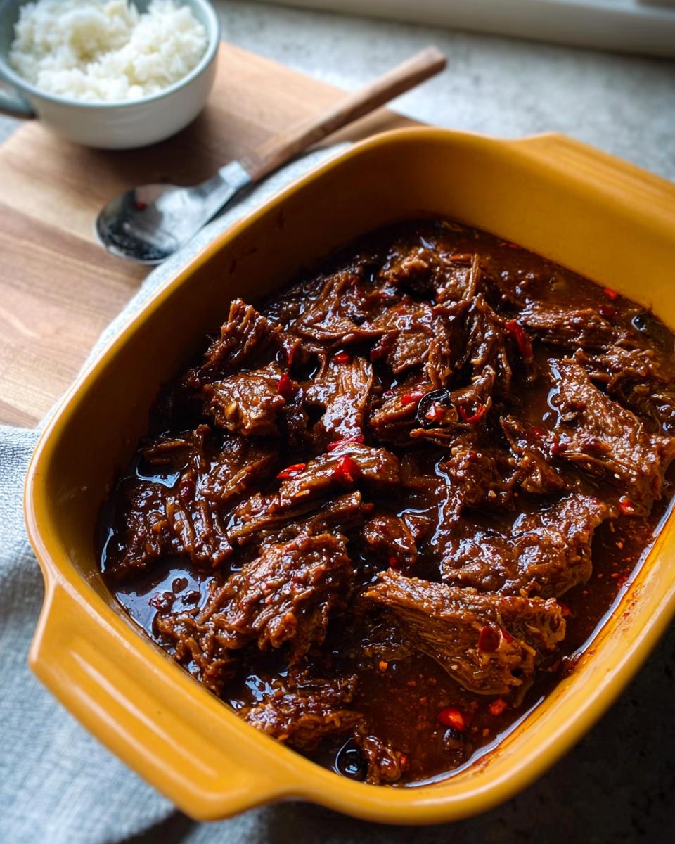 Close-up of tender Korean Style Pot Roast in a yellow dish, with visible chili flakes and a side of white rice.