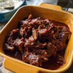 Close-up of shredded Korean Style Pot Roast in a rich, dark sauce with red chili flakes.