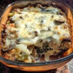 A close-up view of a baked Low Carb Philly Cheesesteak Casserole in a glass baking dish, topped with melted cheese and visible ingredients like mushrooms and peppers.