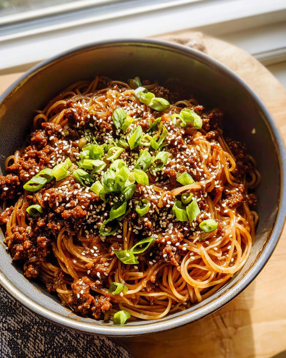 A close-up of a bowl filled with Mongolian Ground Beef Noodles, topped with sesame seeds and chopped green onions.