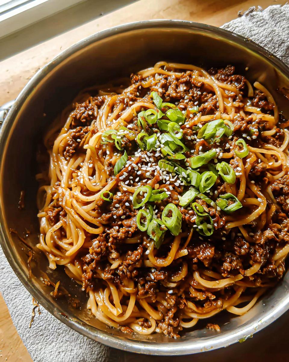 A close-up of a bowl of Mongolian Ground Beef Noodles, topped with green onions and sesame seeds.
