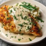 A golden Parmesan crusted chicken breast is smothered in creamy garlic sauce and served with mashed potatoes and green beans.