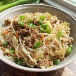 A close-up of a bowl filled with a Potsticker Noodle Bowl featuring ground pork, noodles, cabbage, and green onions.