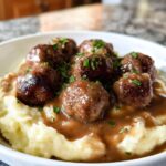 A bowl of Salisbury steak meatballs served over creamy garlic herb mashed potatoes, garnished with fresh parsley.