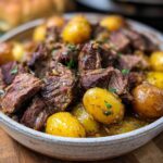 A bowl of tender Slow Cooker Garlic Butter Beef with Potatoes, garnished with fresh herbs.