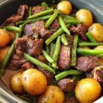 A close-up overhead view of slow cooker garlic butter beef with potatoes and green beans in a crock pot.