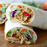 Close-up of a Teriyaki Chicken Wrap cut in half, showing shredded chicken, vegetables, and sauce.