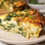 A slice of baked cottage cheese eggs with spinach and scallions, showcasing a fluffy texture and golden-brown crust.