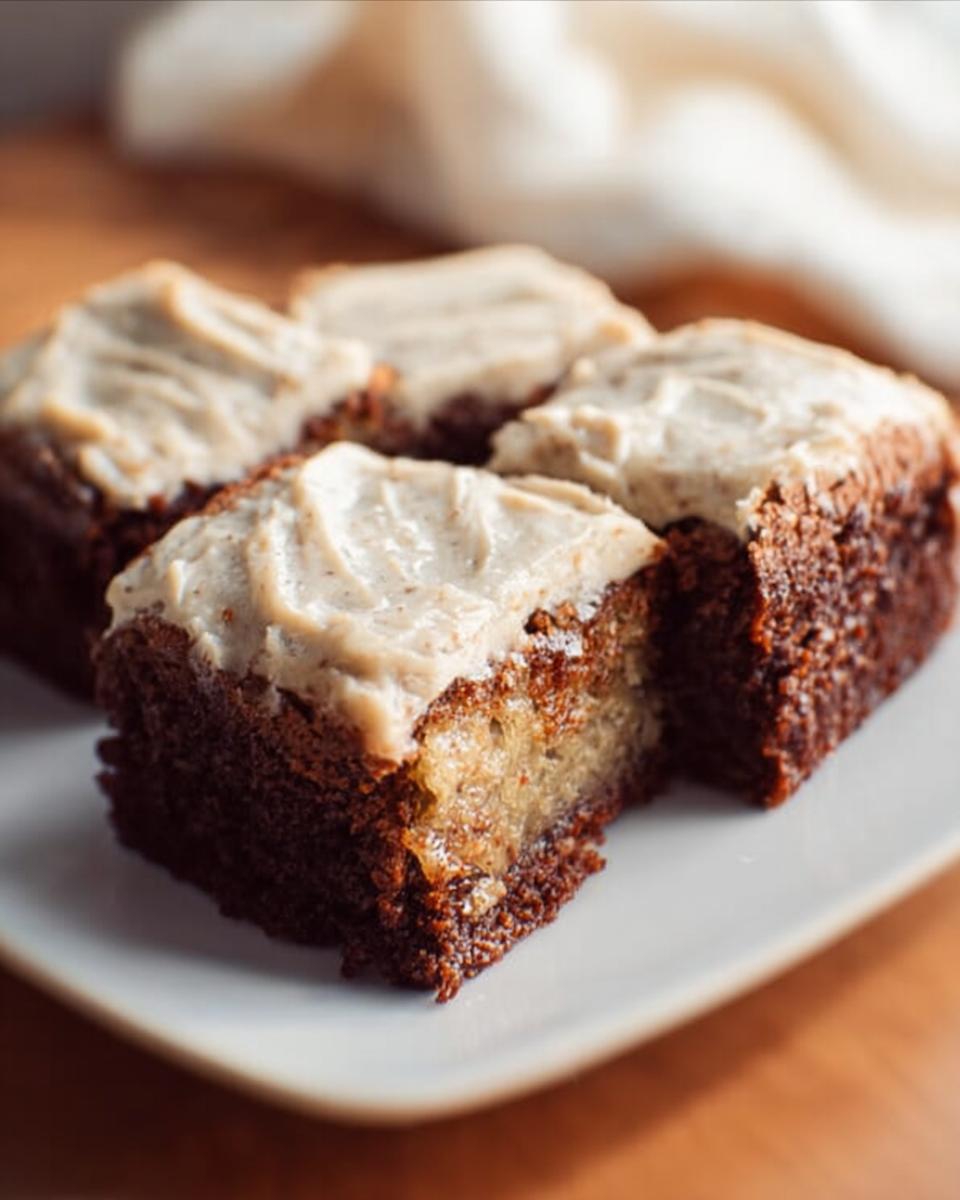 Four rich chocolate Banana Bread Brownies topped with creamy frosting on a white plate.