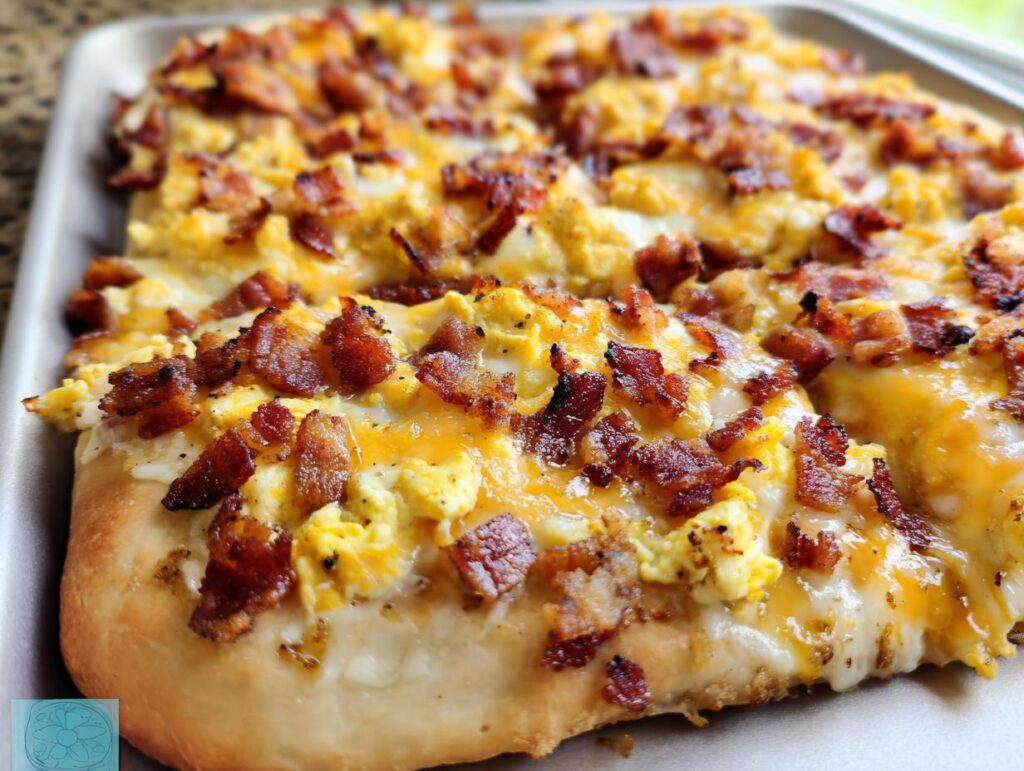 Close-up of a freshly baked breakfast pizza egg recipe topped with scrambled eggs, melted cheese, and crispy bacon.