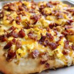 Close-up of a freshly baked breakfast pizza egg recipe topped with scrambled eggs, melted cheese, and crispy bacon.