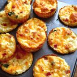 Close-up of golden brown Cheesy Muffin Tin Cottage Cheese Egg Bites in a muffin tin, showing melted cheese and red pepper pieces.