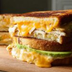 A close-up of a stacked Chicken Avocado Melt Sandwich with melted cheese and avocado slices.