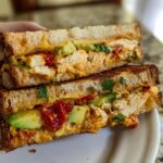 A close-up of a stacked CHICKEN AVOCADO MELT SANDWICH with toasted bread, creamy avocado, shredded chicken, and sun-dried tomatoes.
