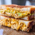 A close-up of a stacked Chicken Avocado Melt Sandwich, showing melted cheese, shredded chicken, and avocado.